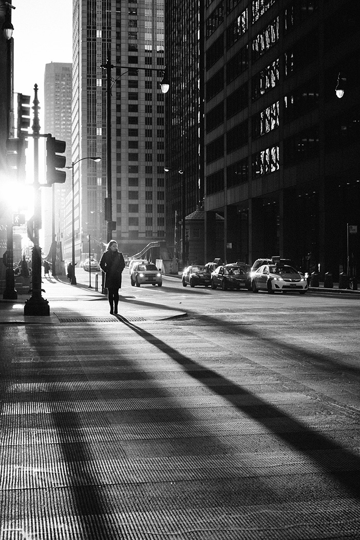 A silhouetted person crosses a city road while the sun streams through the skyscrapers (black & white)