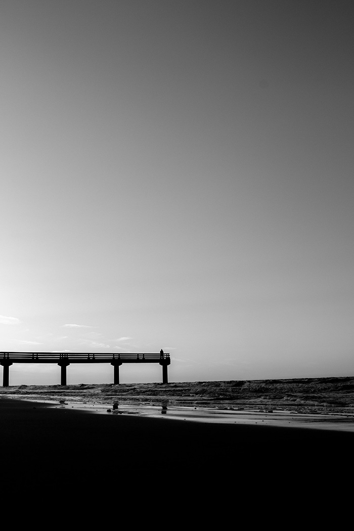 A beach streatches towards the pier in the distance (black & white)