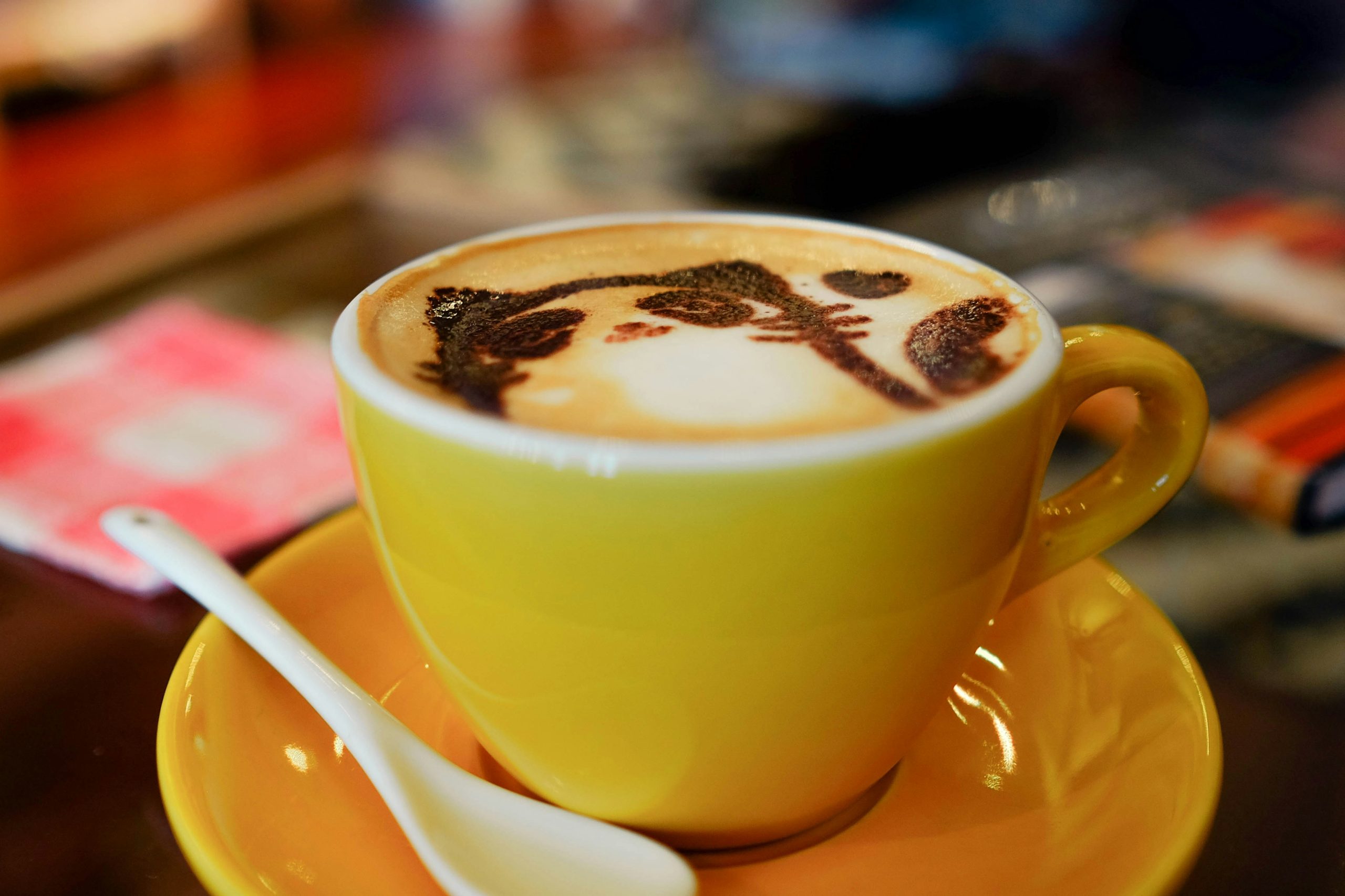 Latte art of a cat in a yellow ceramic mug