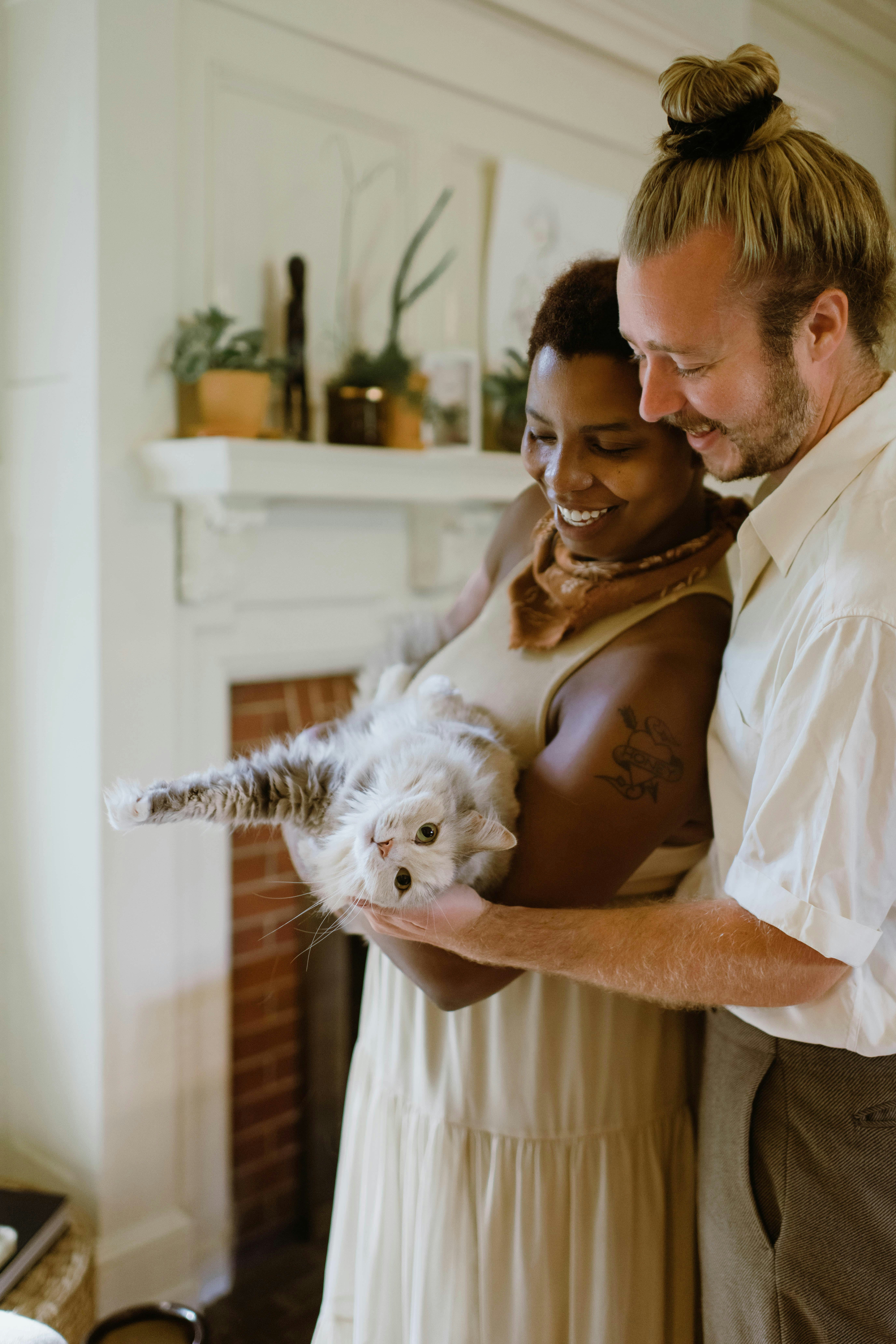 An interracial couple holds their fluffy white cat