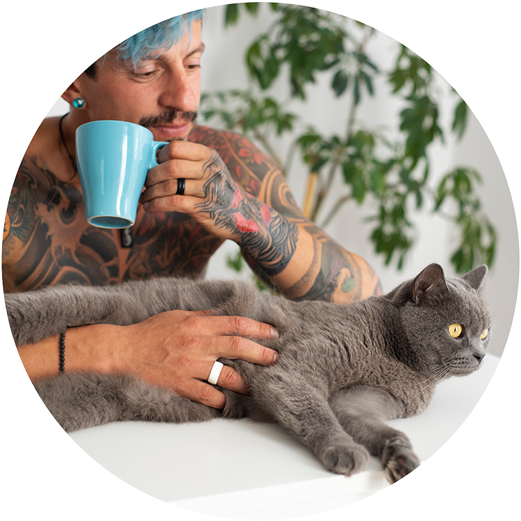 Blue-haired man petting his grey cat while drinking coffee from a blue ceramic mug