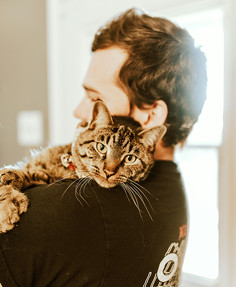 Man holding his cat (ginger tabby adult) on his shoulder - side profile